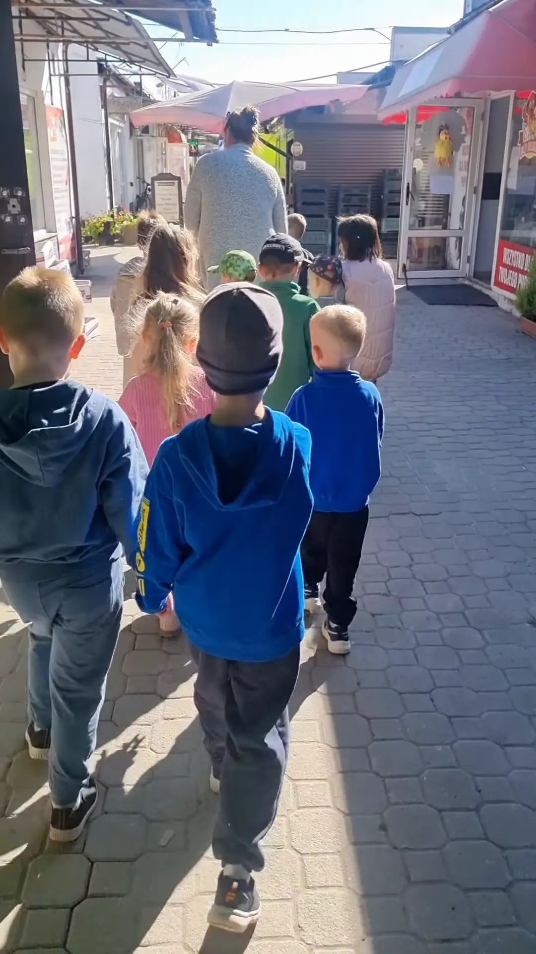 Przedszkolaki idą na zakupy alejką bazarku