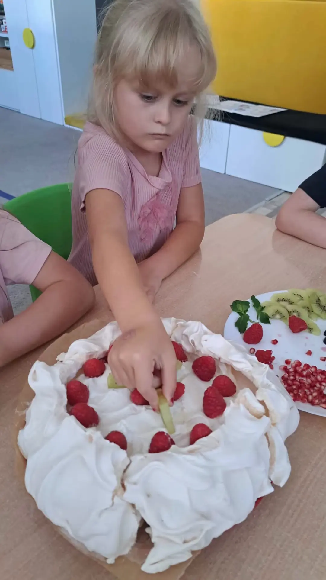 Dziewczynka dekoruje bezę malinami na zajęciach kulinarnych w przedszkolu